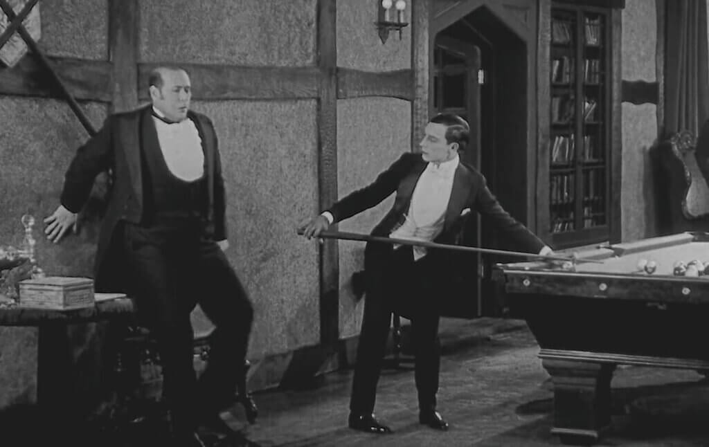 Buster Keaton’s projectionist gestures toward Kathryn McGuire while they sit together in a parlor in Sherlock Jr.
