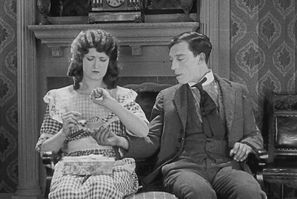 Buster Keaton faces a man beside a billiard table during a comic confrontation in Sherlock Jr.
