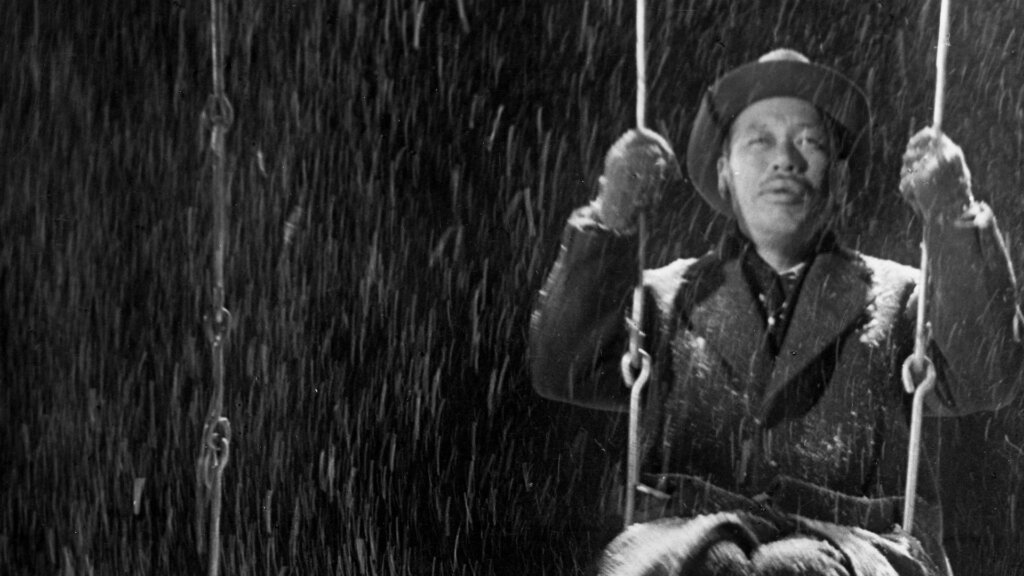 Kanji Watanabe sits on a playground swing in falling snow in Ikiru