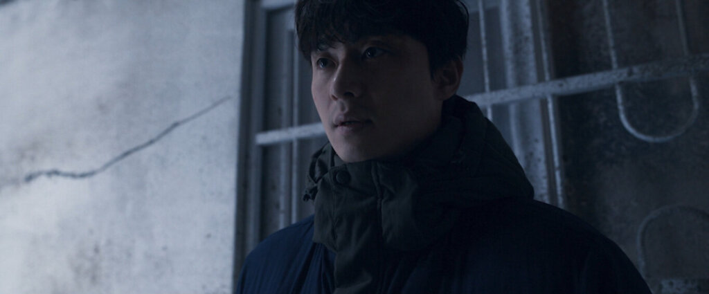 Min-sung stands inside the darkened Hwang Gung apartment building in Concrete Utopia