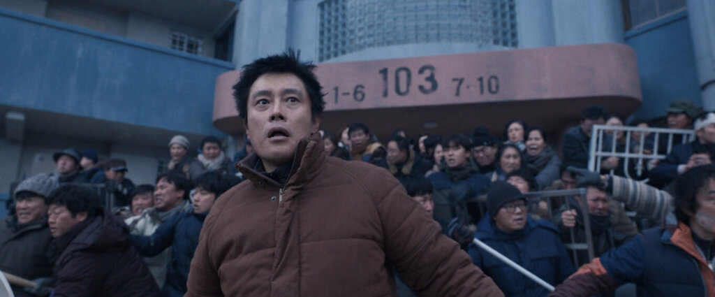 Young-tak stands before residents gathered outside Hwang Gung Apartments in Concrete Utopia