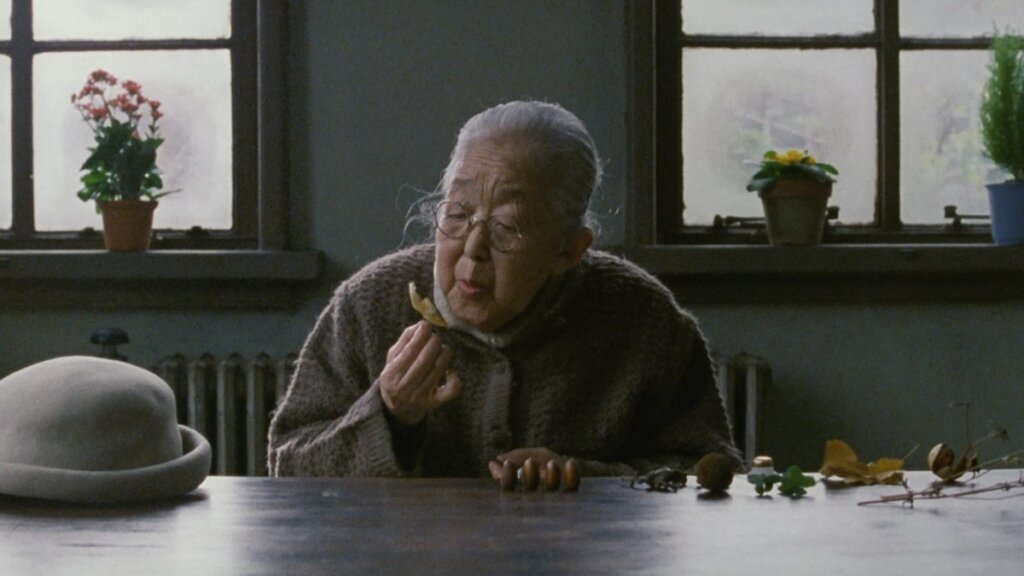 An elderly woman studies a leaf while choosing a memory in After Life