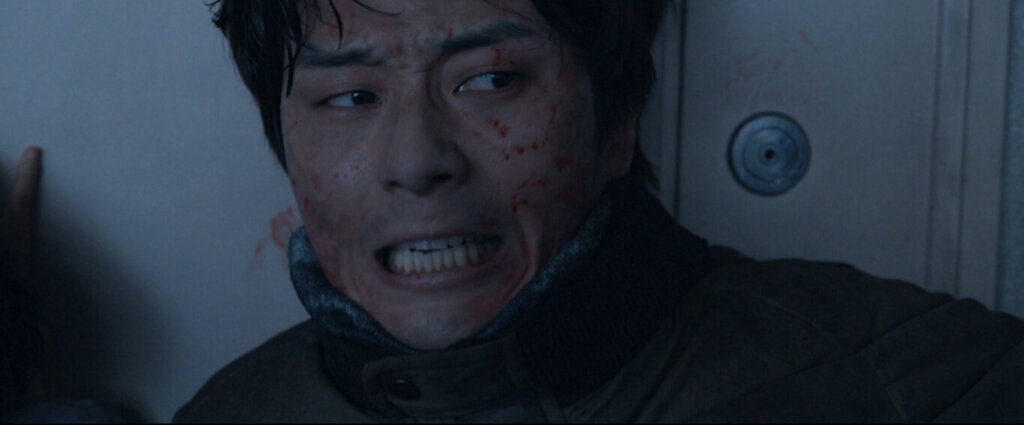 A bloodied Min-sung braces himself against an apartment door in Concrete Utopia