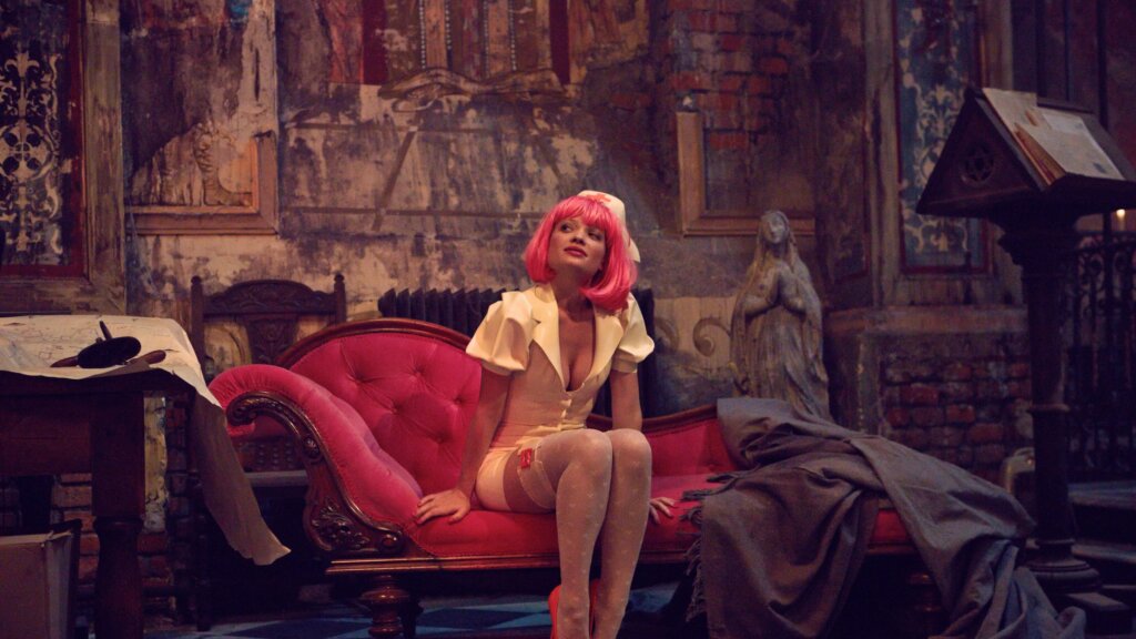 Qohen Leth sits in a pink wig on a red chaise inside his crumbling chapel in The Zero Theorem