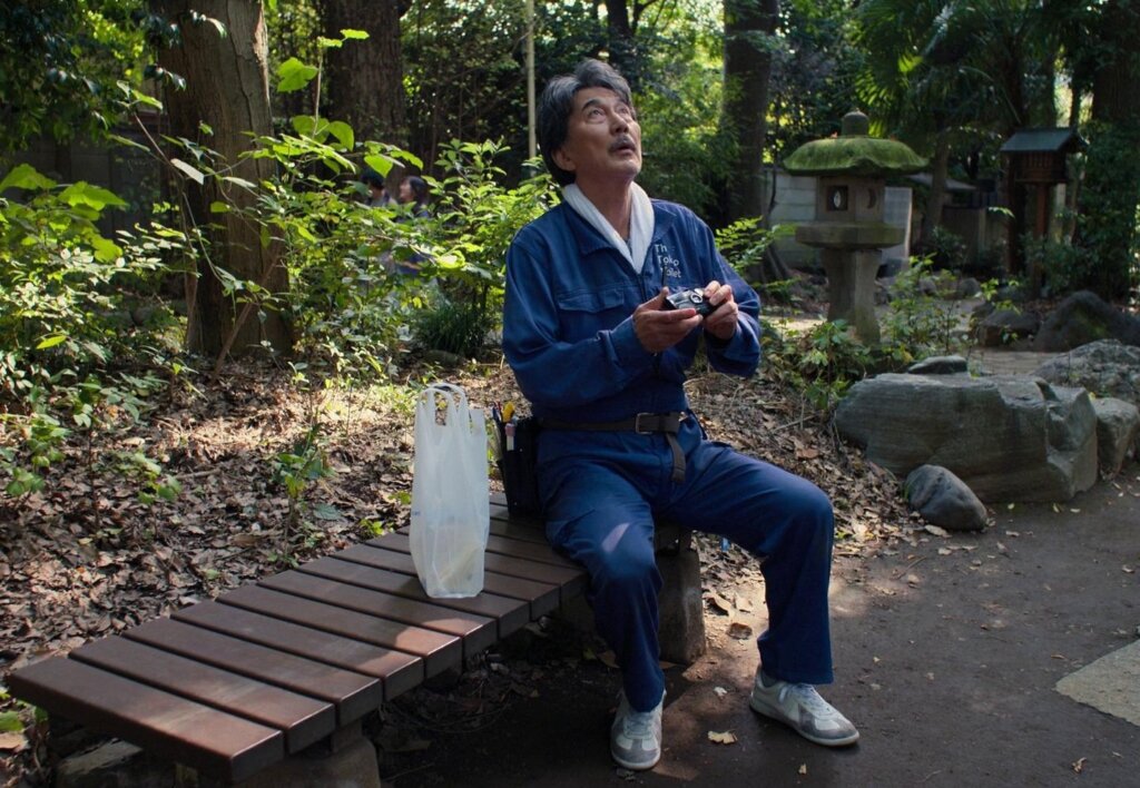Hirayama sits beneath the trees with his camera in Perfect Days