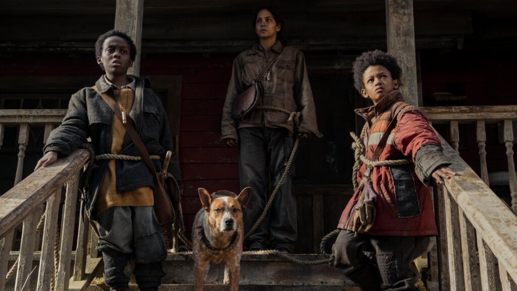 Momma stands behind Nolan, Samuel, and their dog on the cabin porch in Never Let Go.