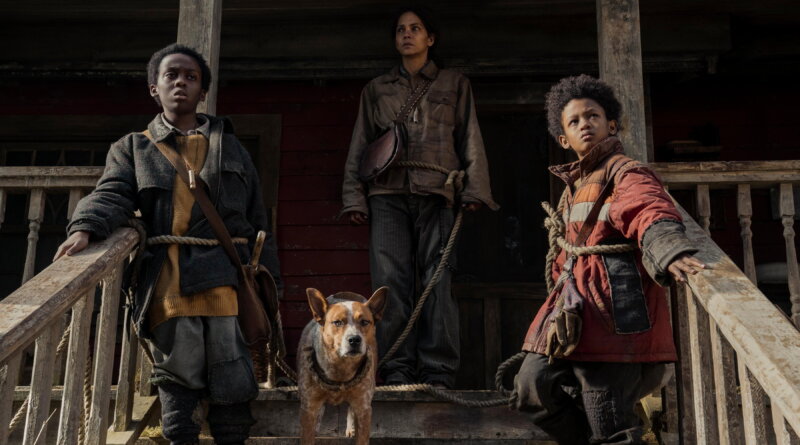 Momma stands behind Nolan, Samuel, and their dog on the cabin porch in Never Let Go.