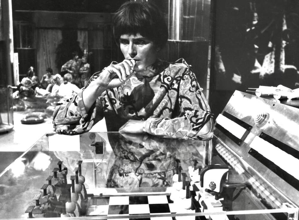 

A television programmer studies a miniature set from behind a glass control console in The Year of the Sex Olympics.