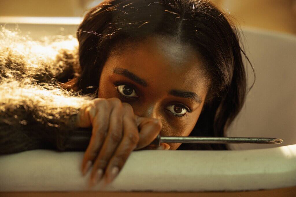 Ariel Ecton peers over a chair while holding a screwdriver in Opus (2025)