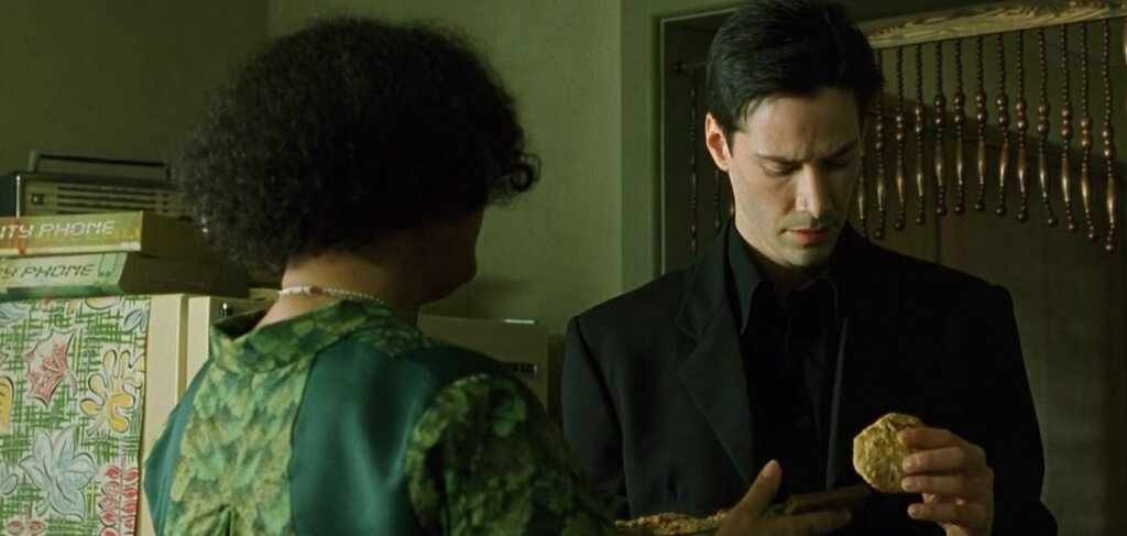 Neo considers a cookie while speaking with the Oracle in her kitchen in The Matrix.