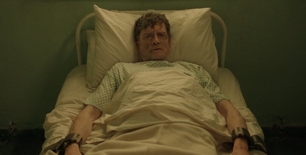 A frightened patient lies restrained in a stark hospital room in Oddity