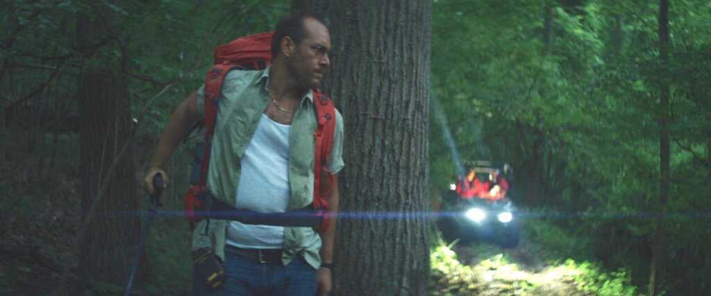 Ray pauses in a forest as an automated cabling machine approaches behind him in Lapsis.