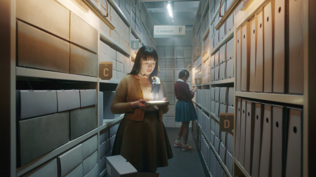 Paula holds a glowing object in an archive corridor lined with labeled film files in The Ordinaries.
