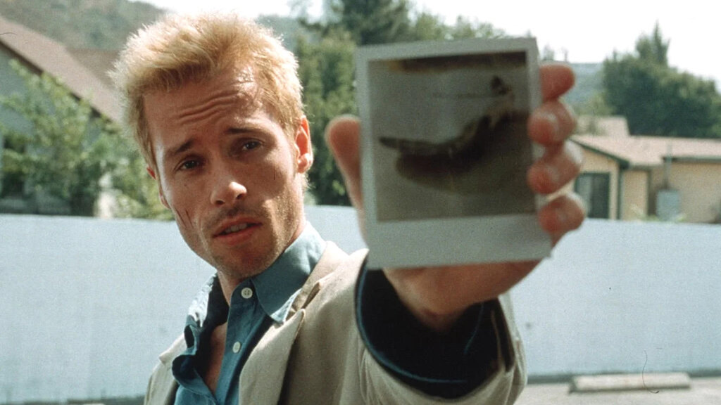Leonard Shelby holds a Polaroid photograph toward the camera in Memento (2000).