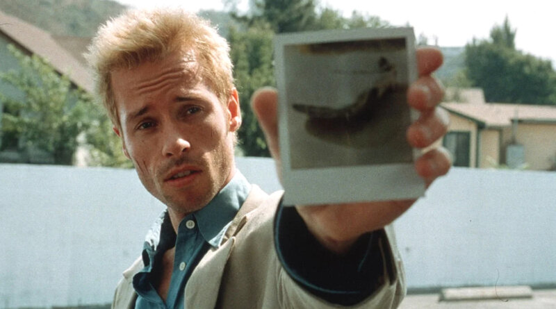 Leonard Shelby holds a Polaroid photograph toward the camera in Memento (2000).