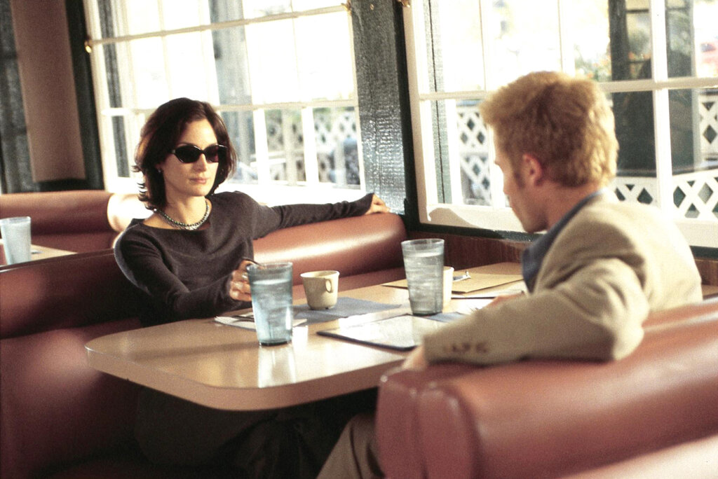 Natalie and Leonard sit across from each other in a sunlit diner in Memento (2000).