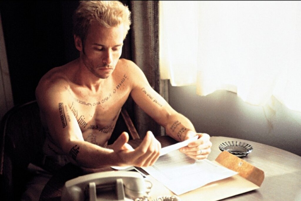 A tattooed Leonard Shelby studies a handwritten note beside his telephone and documents in Memento (2000).