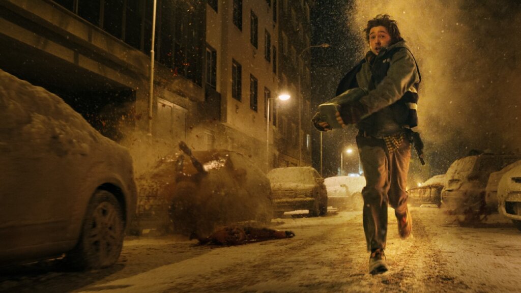 Bryan runs through a snow-covered Raccoon City street as debris erupts behind him in Resident Evil (2026).