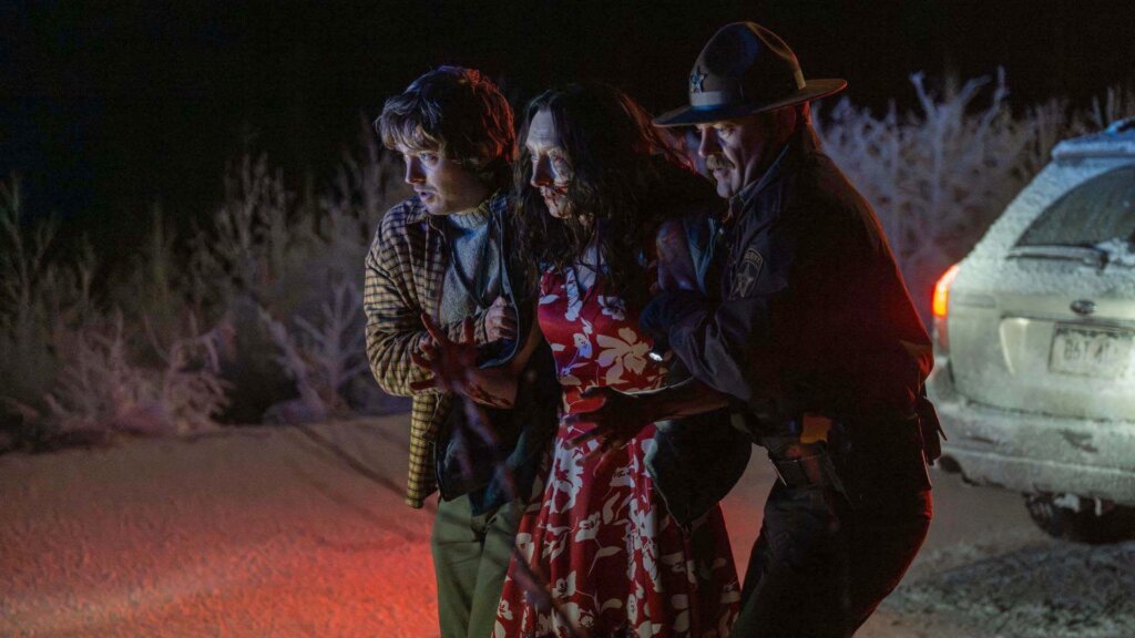 Bryan and a police officer support an injured woman beside a car at night in Resident Evil (2026).