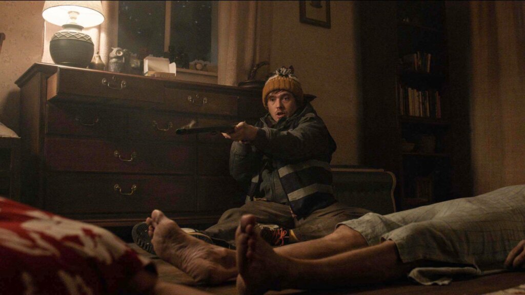 Bryan aims a shotgun across a farmhouse room while a body lies in the foreground in Resident Evil (2026).