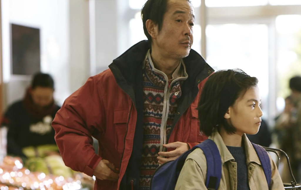 Osamu and Shota perform their practiced shoplifting routine in a crowded market in Shoplifters (2018).