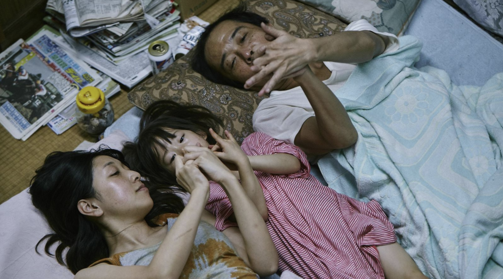 Osamu, Nobuyo, and Yuri lie together and play with their hands inside the family home in Shoplifters (2018).