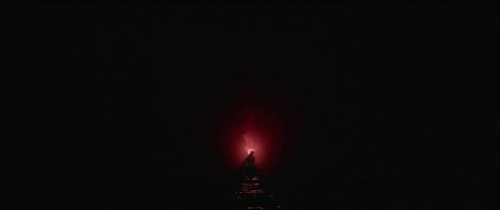 The sea creature rises as a dark silhouette in the ocean against the red glow of a flare in Sweetheart (2019)