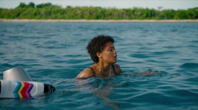 Jenn swims beside a floating suitcase with the island shoreline behind her in Sweetheart (2019).