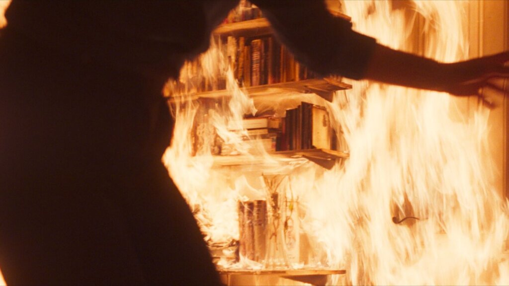 A silhouetted crew member reaches toward the burning film set in Hysteria (2025).