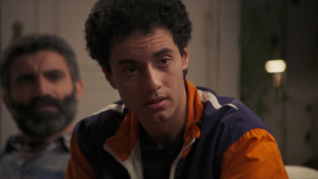 Said speaks while Mustafa watches from behind him in Hysteria (2025).