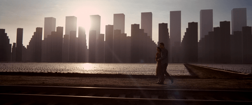 Cobb and Mal walk beside railway tracks beneath the skyline of their dream city in Inception (2010).