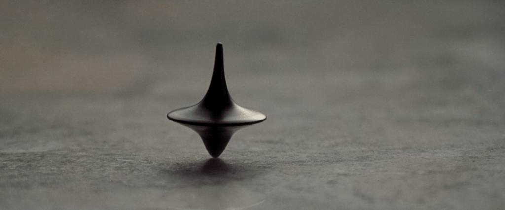 A metal spinning top balances on a gray tabletop in Inception (2010).