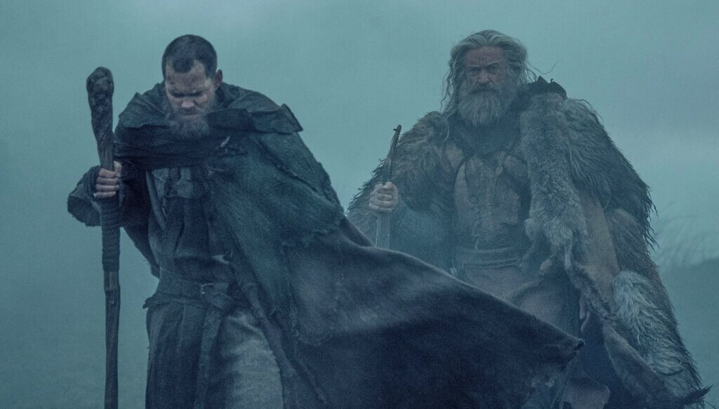 Robin and Little John move through heavy mist behind a horse.