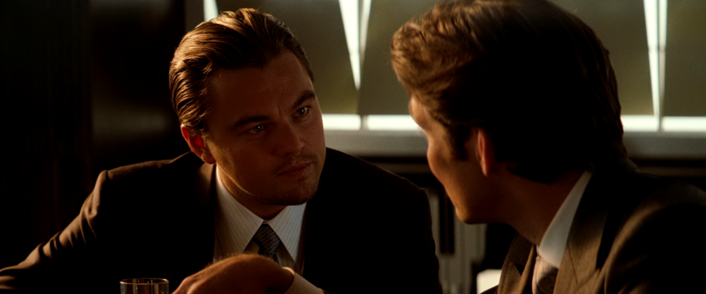 Cobb leans toward Robert Fischer during their conversation in the dream hotel bar in Inception (2010).