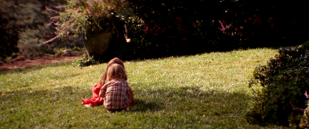 Cobb’s children sit together on the sunlit lawn with their backs to the camera in Inception (2010).
