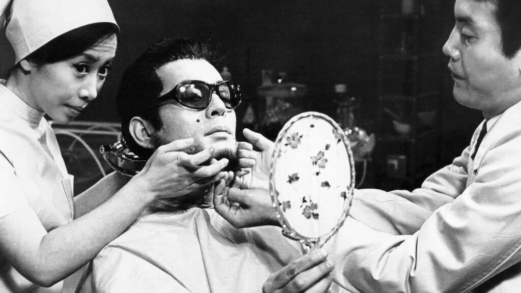 Okuyama looks into a mirror while his mask is fitted in The Face of Another.