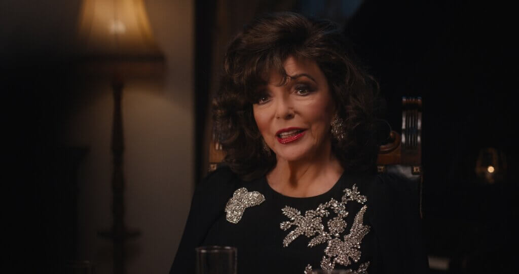 Francesca Carlyle (Joan Collins) sits in an ornate chair wearing a black outfit with sparkling brooches in A Murder Between Friends (2026).