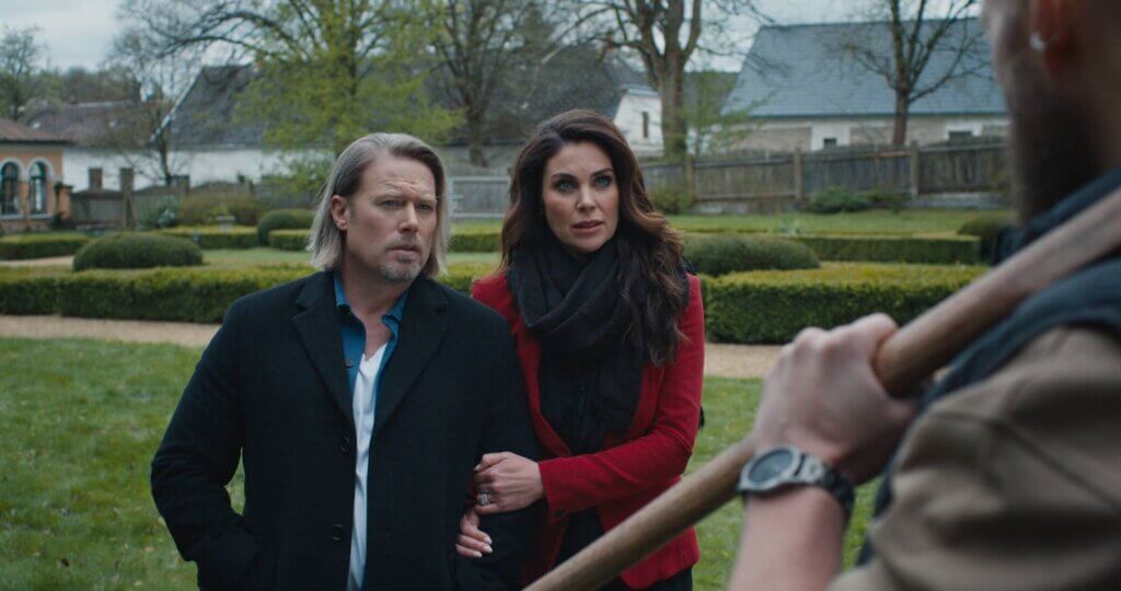 Josh (Jacob Young) and Kat (Nadia Bjorlin) stand arm in arm in the estate gardens in A Murder Between Friends (2026).