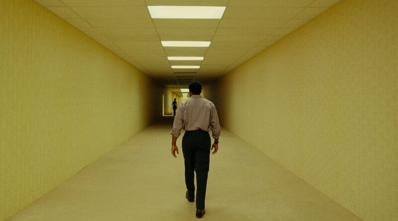 Clark walks toward a distant figure along a yellow corridor beneath fluorescent lights in Backrooms (2026).
