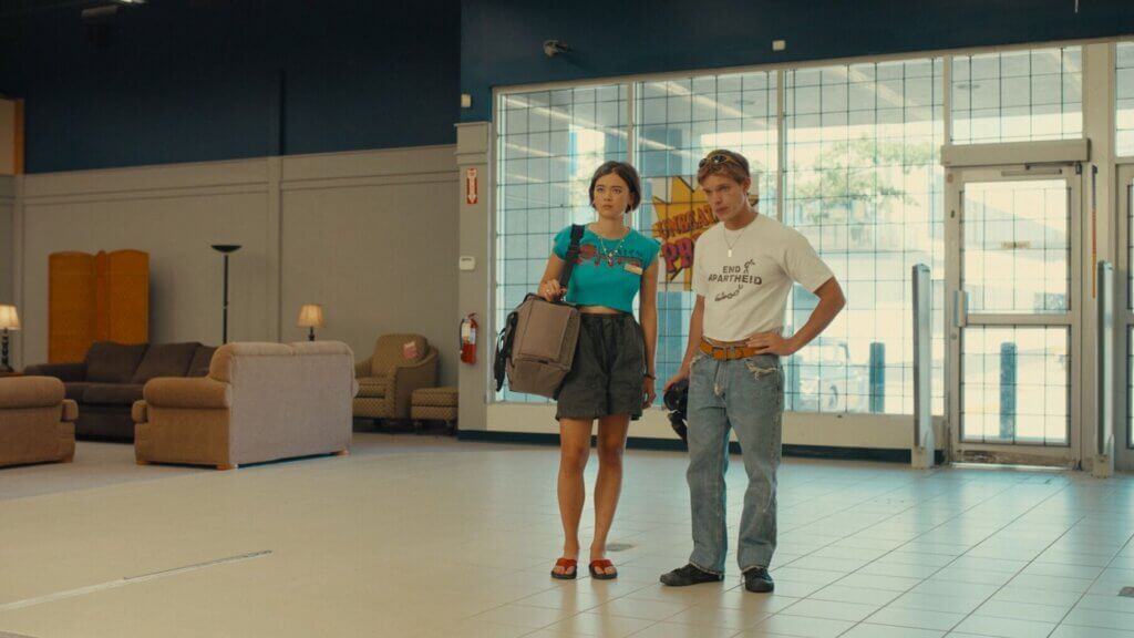 Kat and Bobby stand near the glass entrance of Clark’s furniture showroom in Backrooms (2026).