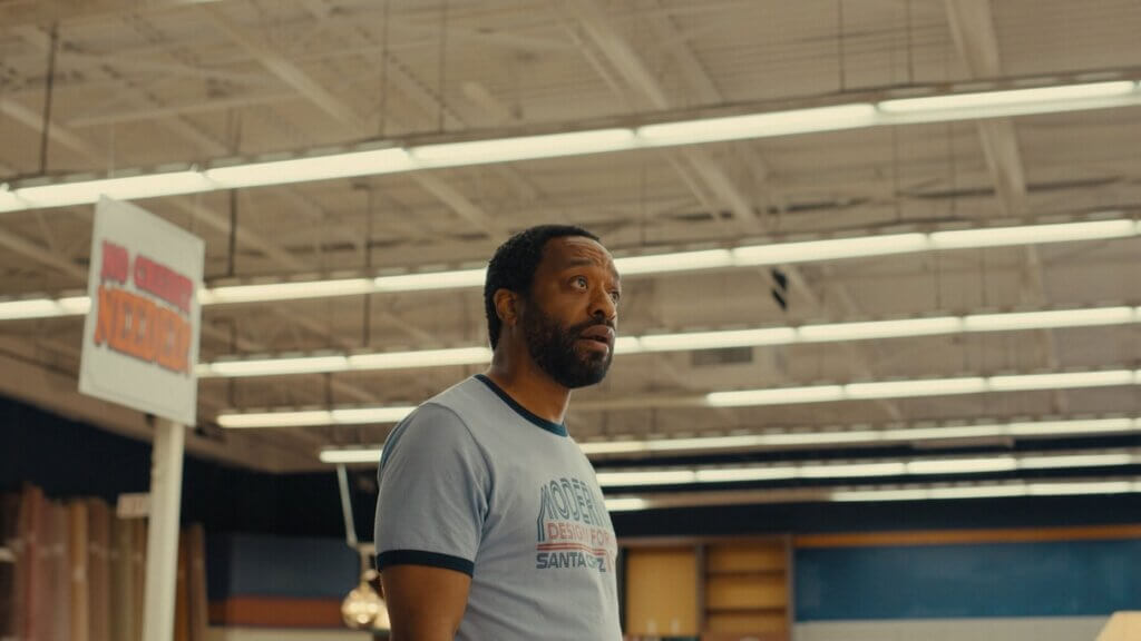 Clark looks across his furniture showroom beneath exposed ceiling beams and fluorescent lights in Backrooms (2026).