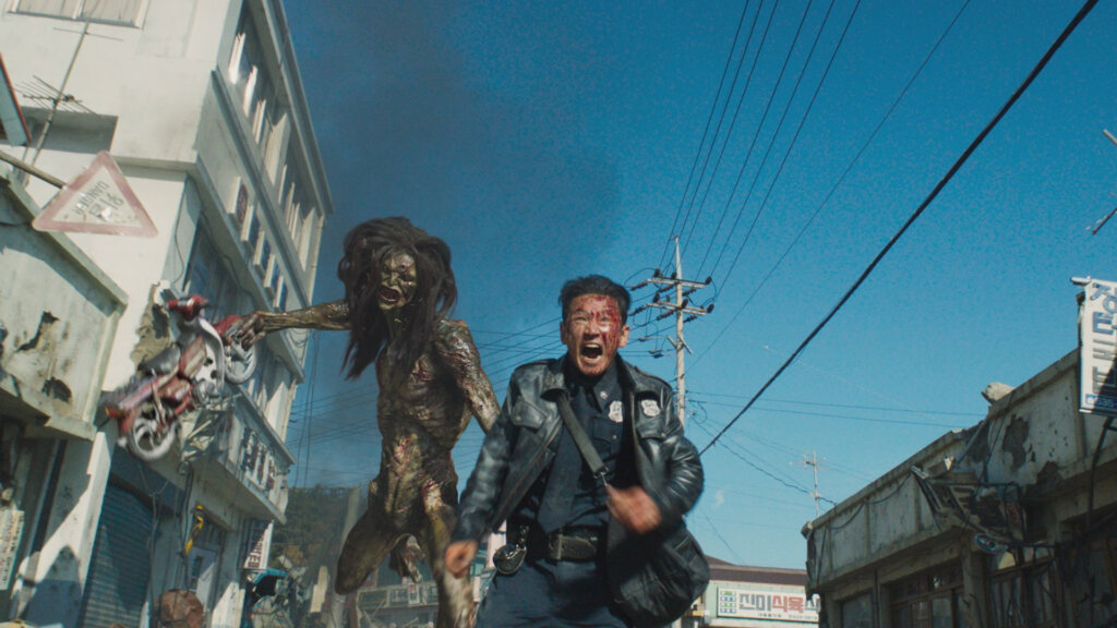 Bum-seok flees along a village street as an alien lifts a motorcycle behind him in Hope (2026).