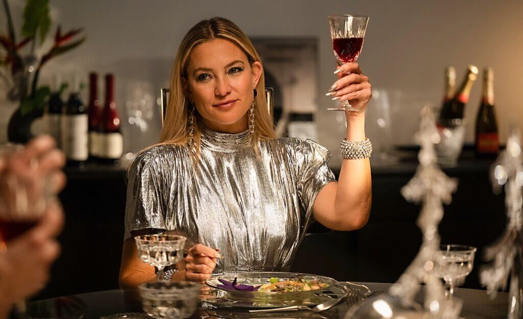 shell-2025-02-zoe-wine.jpg	Zoe Shannon (Kate Hudson), wearing a silver dress, raises a glass of red wine at a dining table in Shell (2025).